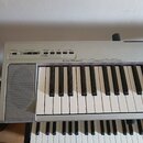 Stříbrný digitální klavír s bílými a černými klávesami. Na horním panelu jsou nápisy STRANDBY ON, MASTER VOLUME, METRONOME ON/OFF, SONG, GRAND PIANO…