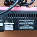 Zadní strana červeného elektronického nástroje s černým plastovým šasi. Na zařízení jsou viditelné nápisy „Power on/off“, „SERIAL NUMBER“ a štítek s…