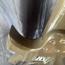 Detailní pohled na zadní část trupu elektrické kytary v béžové nebo šampaňské barvě. Je vidět spoj hnedbá krku s tělem a čtyři kovové šrouby uvnitř v…