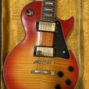 Elektrická kytara typu Les Paul s červeno-žlutým sunburst povrchem a viditnou strukturou dřeva. Nástroj má dva krémové humbuckery, zlatý hardware a č…