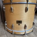 Světle hnědý dřevěný buben s chromovaným kováním. Na korpusu je umístěn černý obdélníkový štítek s nápisem Pearl Mastery Custom. Povrch dřeva vykazuj…