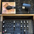 Fotografie zachycuje syntetizátor Moog Labyrinth v originální krabici spolu s napájecím adaptérem a manuálem. Přístroj má tmavě modré tělo s bílými n…