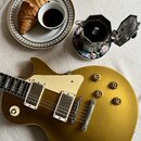 Zlatá elektrická kytara s tvarem singlecut, krémovým pickguardem a dvěma humbuckery. Na kytaru jsou vidět drobné škrábance a opotřebení povrchu. Vedl…