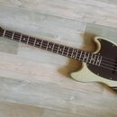 Elektrická basová kytara s bílým třpytivým povrchem těla a černým pickguardem. Na hlavě hmatníku je bílý nápis Squier Mustang Bass. Nástroj má tmavý…