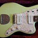 Světle zelená elektrická kytara v červeném plišovém pouzdře. Nástroj má perleťový pickguard, dva snímače s bílými kryty a kovový most s integrovaným…
