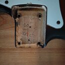Detailní pohled na zadní část kytary s vyjmutým krytem elektroniky. V dutině je vidět dřevo s nápisem SJS a červeným znakem. Okraje dutiny vykazují o…