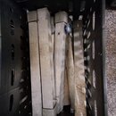 Černý plastový přepravní box, ve kterém jsou naskládané kovové profily stříbrné barvy. Povrch kovových částí vykazuje známky opotřebení a znečištění.…