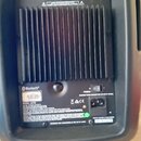 Zadní strana černého akustického komba s ventilační mřížkou. V horní části jsou tři vstupy s nápisy MIC/LINE, MIC/LINE a MIX OUT a ovratový knoflík B…
