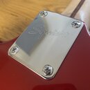 Detail červeného trupu elektrické kytary s nerezovým krytem elektroniky. Na kovovém krytu je vyryt nápis Squier®. Kryt je připevněn čtyřmi křížovými…