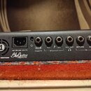 Záběr na zadní panel černého kytarového zesilovače. Na zařízení jsou nápisy IRIDIUM EDITION a logo BluGuitar TONE INNOVATION. Panel obsahuje napájecí…