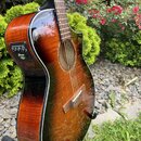 Akustická kytara s cutawayem v červenohnatém sunburst provedení s vysokým leskem. Na boku korpusu je umístěn ovládací panel s nápisem Ibanez a řadou…
