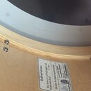 Detail dřevěného korpusu basového bubnu světlé barvy. Na korpusu je nalepený bílý štítek s nápisy: Hallvad drums, Bass drum 22"x18" 6 ply maple / ash…