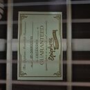Detailní pohled do otvoru akustické kytary s viditelnou štítkem. Na štítku je uveden nápis This Epiphone Masterbilt Instrument, Model EF-500RCCE/NS a…