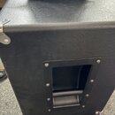 Detailní pohled na roh černého reproduktorového boxu s povrchem z texturovaného vinylu. Na boku je umístěna čtvercová výřez s integrovanou plastovou…