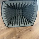Šedý akustický odrazový štít s vnitřním povrchem z pyramidového akustického pěnového materiálu. Štít má obdélníkový tvar se zaoblenými rohy a černý t…