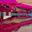 Tmavě červená elektrická kytara typu Les Paul v tvrdém kufru s fialovým polstrováním. Na bílém pickguardu je nápis 1960 a na hlavě hmatníku modrý ští…