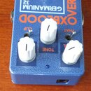 Modrý efekt pedál s nápisy OXBLOOD a OVERDRIVE v oranžové barvě. Na horní části je bílý obdélník s textem GERMANIUM 32. Zařízení má tři bílé plastové…