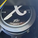 Detailní pohled na zadní část reproduktoru s černým magnetem. Na povrchu je bílé logo ve tvaru stylizovaného písmene X, nápis Peavey a text PEAVEY EL…