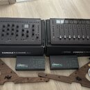 Dvě šedé studiové kontroléry Softube, model CONSOLE 1 CHANNEL Mk III a CONSOLE 1 FADER Mk III. Pod nimi jsou dvě krabice s nápisy Softube CONSOLE 1 C…