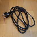 Černý napájecí kabel s evropskou síťovou vidlicí. Kabel je svinutý do smyčky a obsahuje plastový blok pro navijení kabelu. Na povrchu nejsou viditeln…