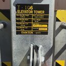 Detailní záběr na kovový profil s černým informačním štítkem. Na štítku je žlutý text T - 106 ELEVATOR TOWER a tabulka s technickými parametry, včetn…