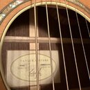 Detailní pohled do otvoru akustické kytary s viditelnými strunami a vnitřním štítkem. Na štítku je uveden nápis TAYLOR GUITARS, model 916ce a sériové…