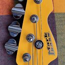 Detail hlavy žluté basové kytary s chromovanými ladičkami. Na povrchu je černý nápis Mark Bass. Instrument vykazuje minimální známky opotřebení, povr…