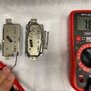 Fotografie zobrazuje dva kovové moduly s vnitřním zapojením a přiloženým digitálním multimetrem značky POWERFIX Profi, který ukazuje hodnotu 7.69. Na…