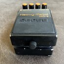 Černý efekt pedál s nápisy Heavy Metal a HM-2. Na horní části je výrazné logo BOSS a čtyři oranžové ovládací knoflíky s popisky OUTPUT a INPUT. Povrc…