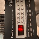 Černý elektronický modul s nápisy Roland a PERCUSSION SOUND MODULE TD-3. Zařízení obsahuje řadu tlačítek, ovládacích prvků a červeně svítící displej.…