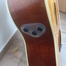 Detail boku akustické kytary s hnědým dřevěným povrchem a krémovým lemováním. V těle je osazen ovládací panel s nápisem TransAcoustic a dvěma černými…