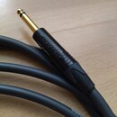 Detailní záběr na konektor 6,35mm jack v černé barvě s pozlaceným hrotem. Na černém plastovém těle je vyražen nápis NEUTRIK. Kabel je tlustý, v tmavě…