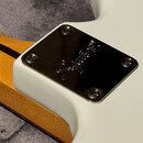 Detailní pohled na bílý krk elektrické kytary s kovovým krytem hmatníku. Na chromovaném krytu je vyražen nápis Squier. Kryt je připevněn čtyřmi šroub…