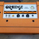 Kytarový zesilovač v oranžovém vinylu s černými plastovými rohy. Na bílém předním panelu je nápis ORANGE TINY TERROR a logo s nápisem "THE AMP FOR TH…