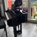 Černý křídlový klavír s vysokým leskem a otevřeným víkem. Na černé lakované ploše nad klávesnicí je vidět nápis "YAMAHA". Nástroj stojí na dřevěné po…