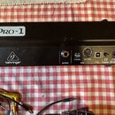 Černý rackový syntetizátor s nápisem PRO-1 na horní části. Na zadním panelu je logo behringer a konektory OUTPUT, MIDI (OUT/THRU), POWER s přepínačem…