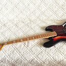 Elektrická basová kytara s korpusem v černo-oranžovém sunburst provedení a javorovým hmatníkem. Na hlavě je nápis "Gretsch" a modelové označení "Elec…