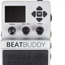 Stříbrný kytarový pedál s digitálním displejem a třemi ovládacími knoflíky označenými Volume, Drum Set a Tempo. V pravé horní části jsou čtyři směrov…