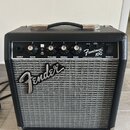 Černý kytarový kombo zesilovač s šedou textilní mřížkou a chromovaným logem Fender. Na ovládacím panelu jsou nápisy Frontman 10G, FENDER MUSICAL INST…