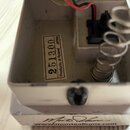 Detail vnitřku šedého efekt pedálu s kovovým šasi. Uvnitř je vidět bílá nálepka s nápisem 251300 Products of Roland JAPAN, červeno-černý kabel a kovo…