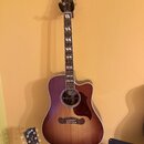 Akustická kytara s cutawayem v tmavě hnědém přechodovém odstínu. Na hlavě je nápis Gibson a na hmatníku jsou bílé vložky ve tvaru obdélníků. V místě…