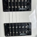 Detail dvou černých humbuckerů s instalací v černých rámečcích na bílém povrchu kytary. Oba snímače mají stříbrné pólové šrouby a bílý nápis Jackson.…