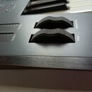 Detailní záběr na ovládací panel černého klávesového nástroje. Jsou vidět dva černé vlnovité ovladače s nápisy MODULATION a PITCH oraz dvě drážky pro…