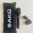 Černý dynamický mikrofon s mřížkou a černým textilním pouzdrem. Na pouzdře je bílý nápis AKG s logem, na těle mikrofonu je logo a ve spodní části náp…