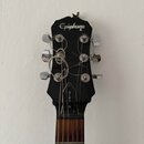 Fotografie zachycuje hlavu kytary černé barvy s nápisem Epiphone na horní části. Na zadní straně krku je svisle napsáno GIBSON. Ladicí kolíky jsou ch…