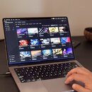 Otevřený notebook v šedé barvě s rozsvícenou klávesnicí. Na displeji je zobrazen software Native Access s přehledem instalovaných knihoven a nástrojů…