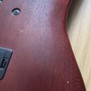 Detailní pohled na zadní stranu dřevěného korpusu nástroje v tmavě červeně hnědé barvě. Povrch vykazuje drobné škrábance a opotřebení laku. V horní č…