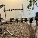 Chromovaný kovový stojan na perkuse nebo bicí s několika horizontálními a vertikálními tyčemi. Na různých částech konstrukce jsou vidět nápisy Gibral…