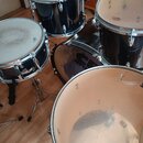 Sada černých bubnů s kovovými obručemi. Na blanách jsou vidět loga „Remo“ a nápisy „UX PURE HEADS MADE IN TAIWAN“. Povrch blan vykazuje známky opotře…