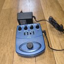 Modrá kytarová stupňová pedál s nápisem GUITAR GDI 21 a logem behringer. Zařízení má čtyři ovládací knoflíky s popisky DRIVE, TREBLE, BASS a LEVEL, n…